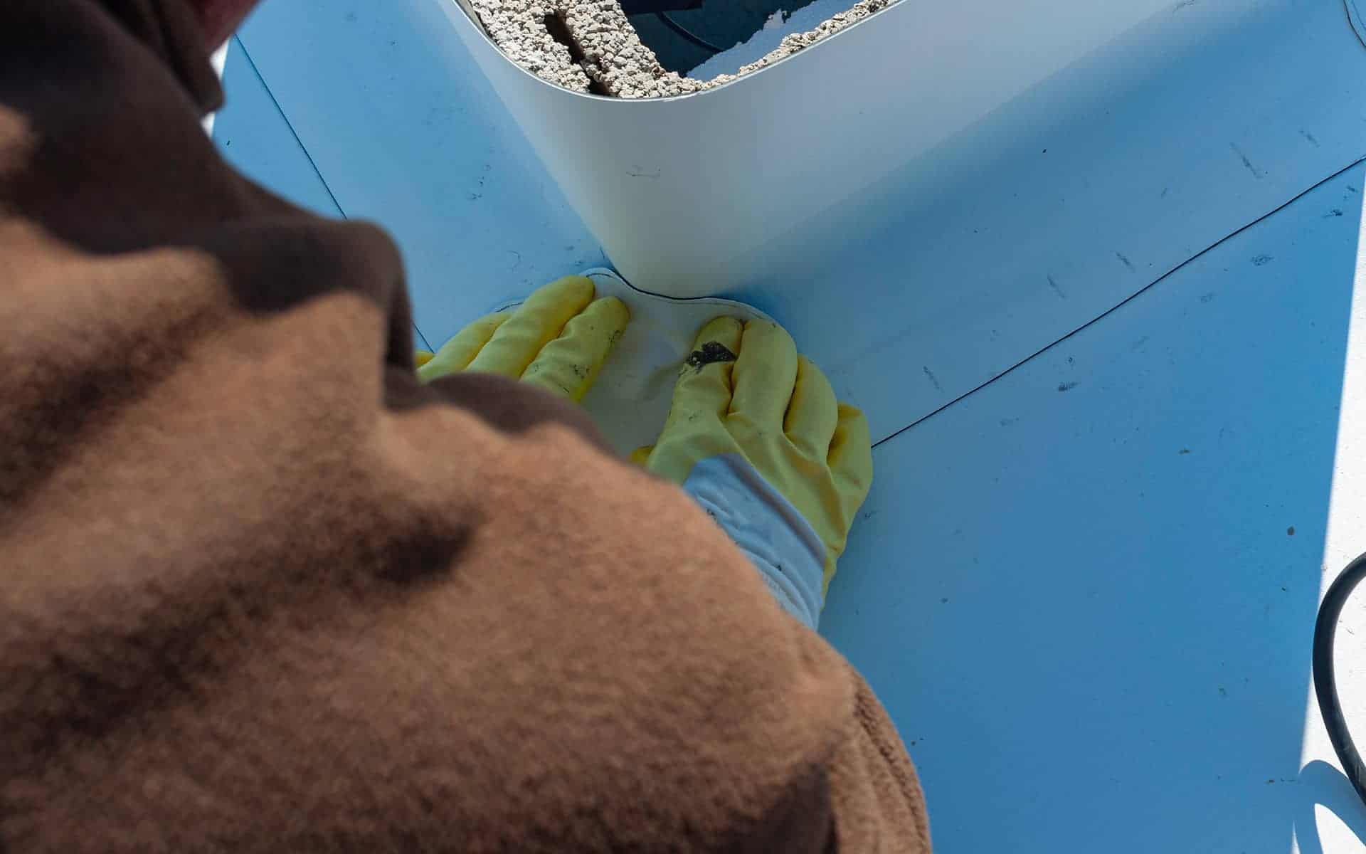 Close-up of a gloved worker applying a patch to a white commercial roof corner.